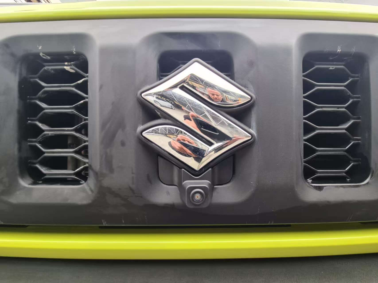 Front camera mounted below the Suzuki badge in a lime-green off-road vehicle grille