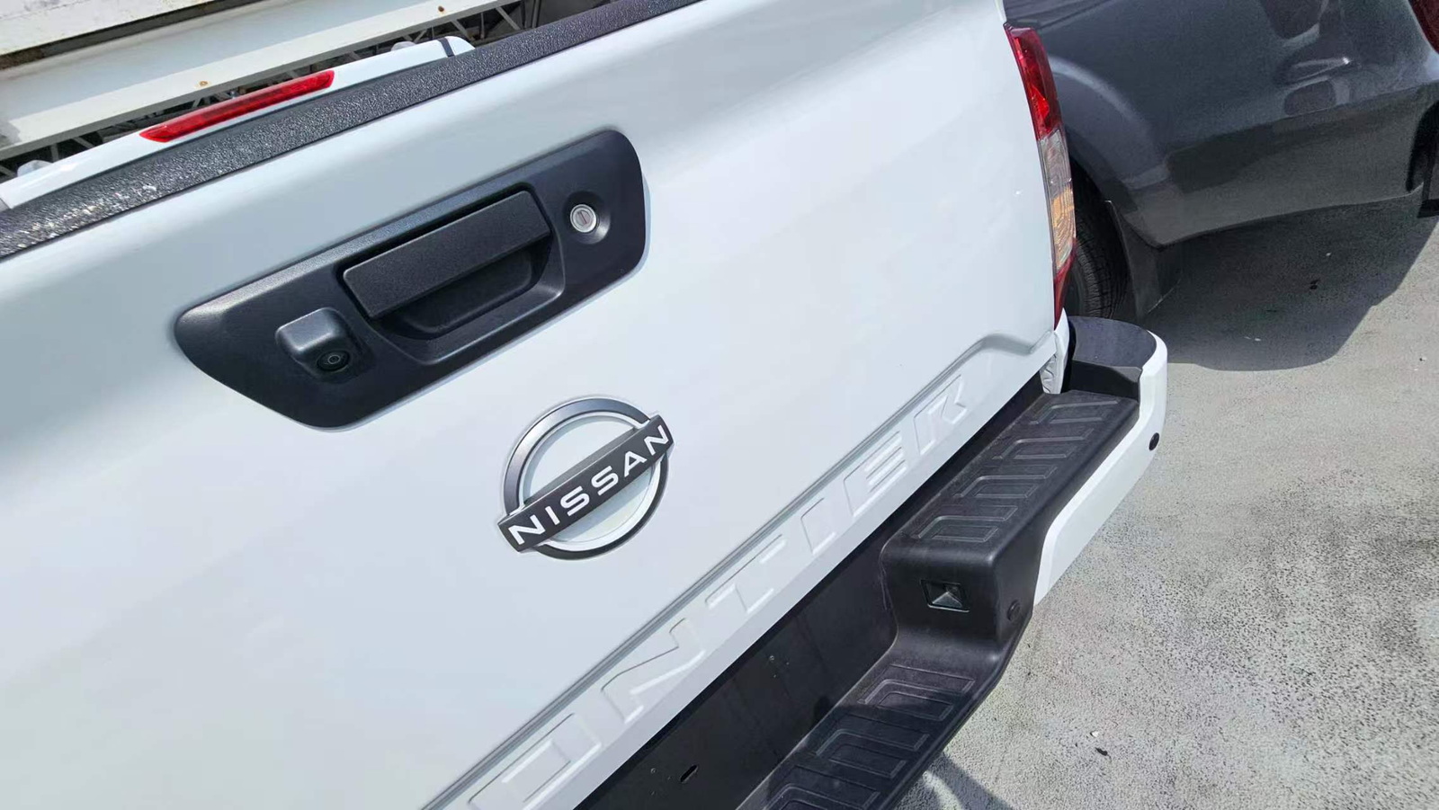 Close view of a camera integrated beside the tailgate handle of a white Nissan pickup